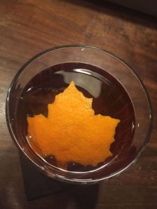Cocktail con garnish de hoja con piel de naranja